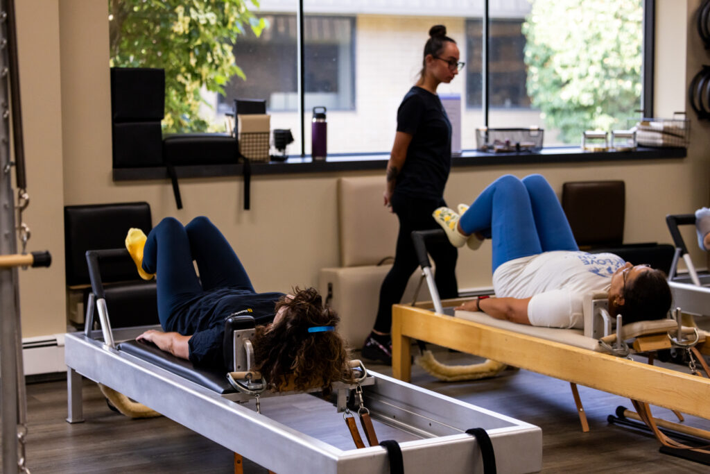Precision Pilates clients performing reformer exercises in a bright, modern studio.